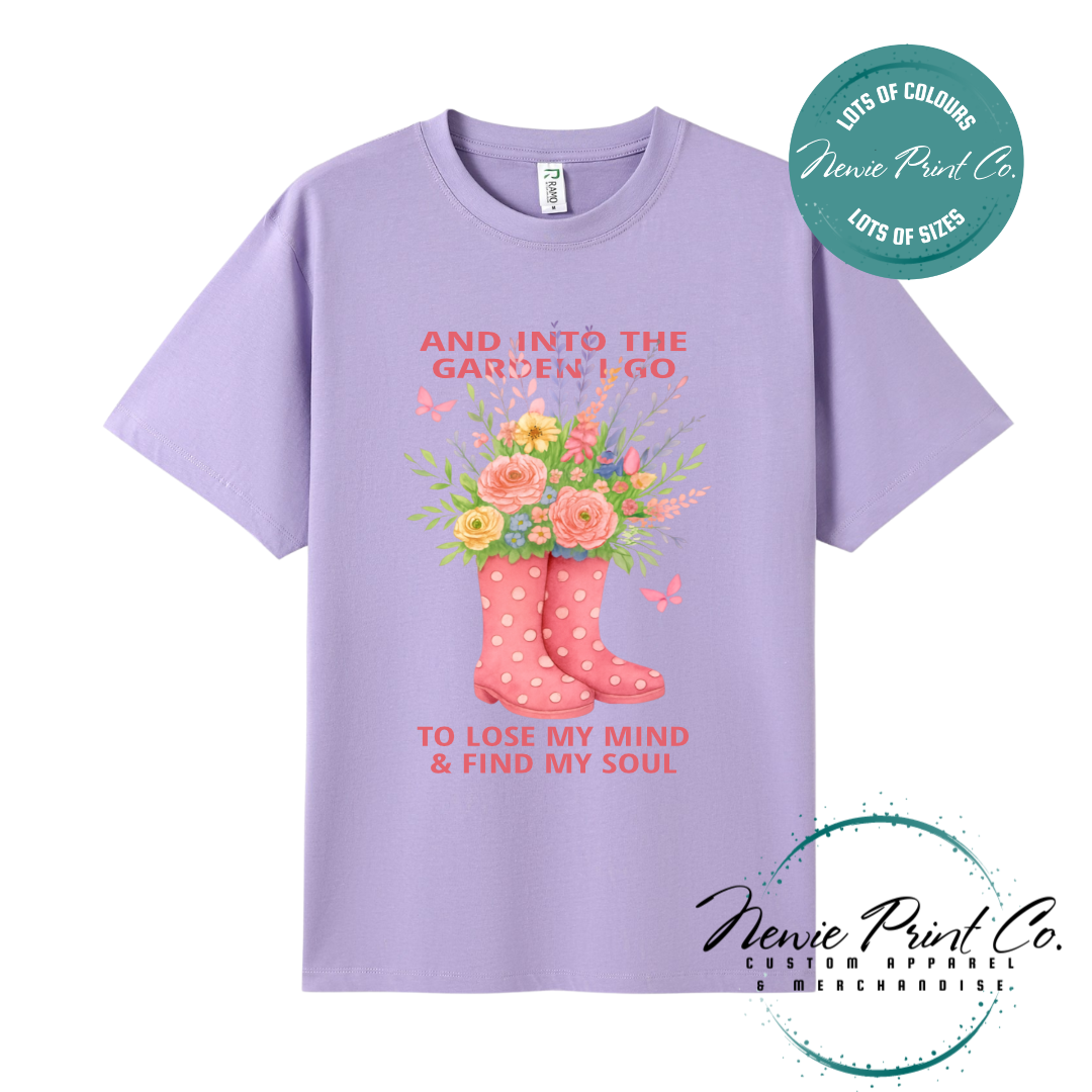“Into the garden I go to lose my mind and find my soul” quote t-shirt featuring a pair of gumboots filled with wildflowers. Whimsical floral garden design printed on 100% cotton tee using high-quality DTF/DTG print, perfect for nature lovers and gardeners.