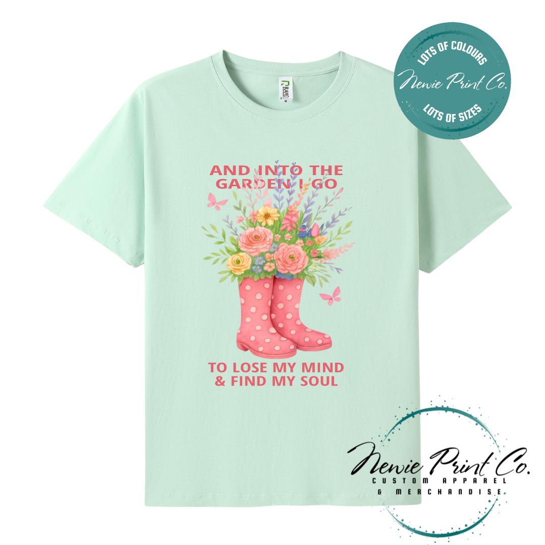“Into the garden I go to lose my mind and find my soul” quote t-shirt featuring a pair of gumboots filled with wildflowers. Whimsical floral garden design printed on 100% cotton tee using high-quality DTF/DTG print, perfect for nature lovers and gardeners.