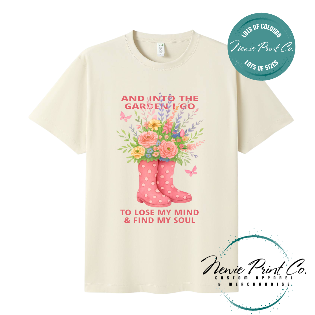 “Into the garden I go to lose my mind and find my soul” quote t-shirt featuring a pair of gumboots filled with wildflowers. Whimsical floral garden design printed on 100% cotton tee using high-quality DTF/DTG print, perfect for nature lovers and gardeners.