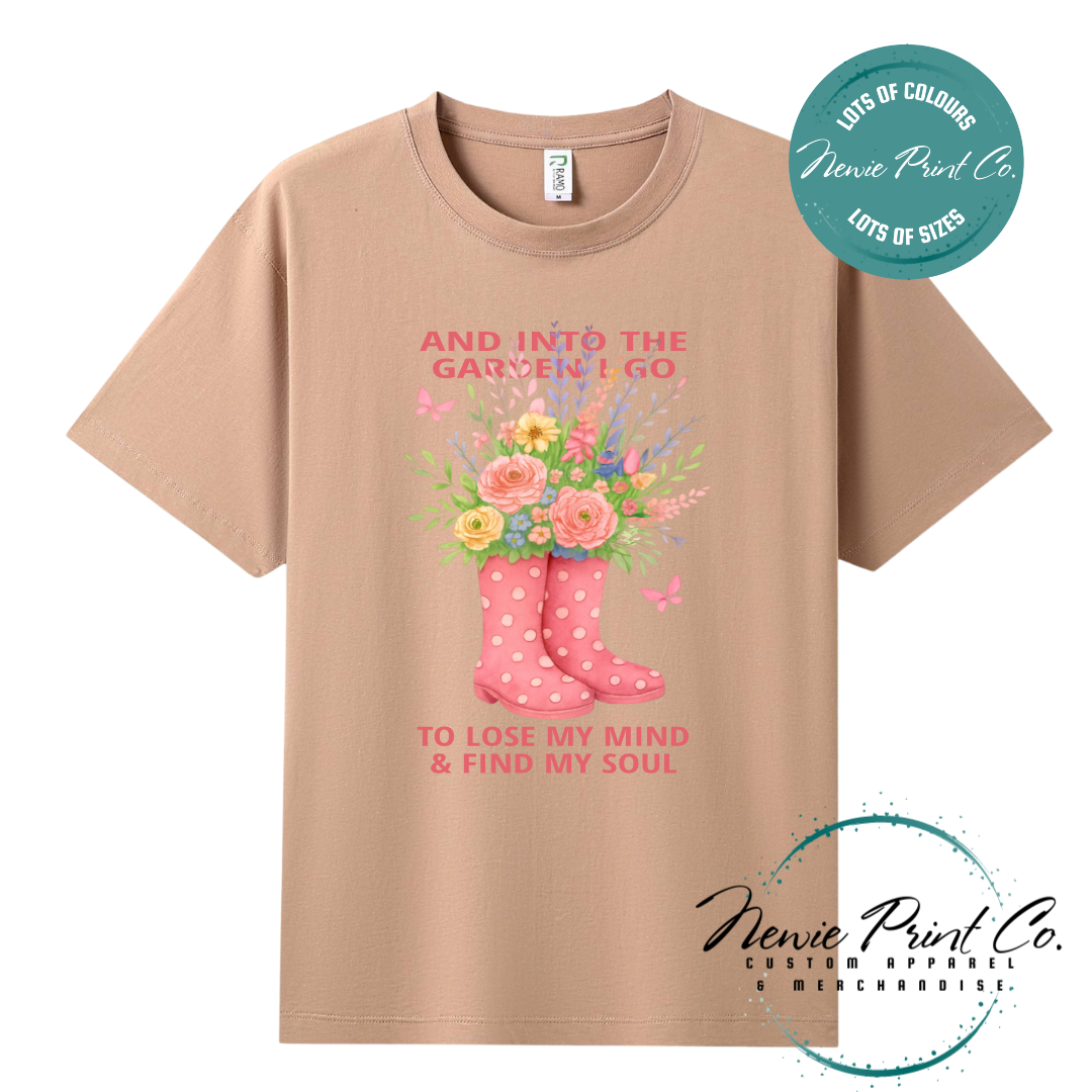 “Into the garden I go to lose my mind and find my soul” quote t-shirt featuring a pair of gumboots filled with wildflowers. Whimsical floral garden design printed on 100% cotton tee using high-quality DTF/DTG print, perfect for nature lovers and gardeners.