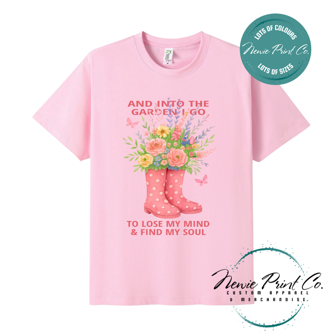 “Into the garden I go to lose my mind and find my soul” quote t-shirt featuring a pair of gumboots filled with wildflowers. Whimsical floral garden design printed on 100% cotton tee using high-quality DTF/DTG print, perfect for nature lovers and gardeners.