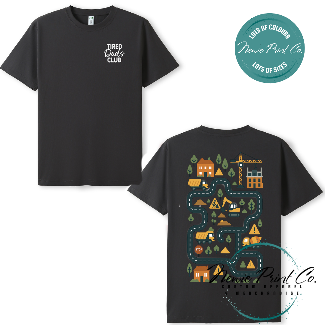 Tired Dads Club black t-shirt featuring front text and a vibrant construction-themed illustration on the back with houses, vehicles, and winding roads. Available in multiple t-shirt colors and various jumper options. Designed and printed by Newie Print Co.