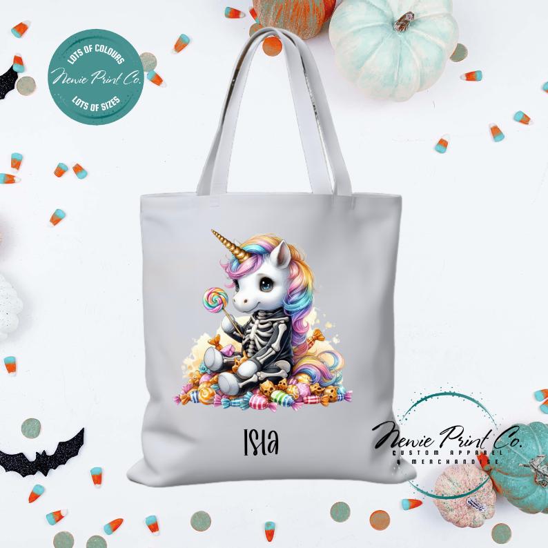 Custom Halloween tote bag with unicorn dressed as a skeleton surrounded by lollies and candy, optional personalised name printed on the front, perfect for trick-or-treating or spooky season gifts