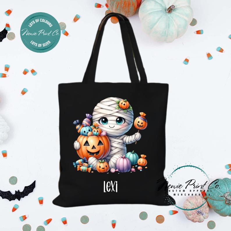 Custom Halloween tote bag with a cute mummy with candy and pumpkins, optional personalised name printed on the front, perfect for trick-or-treating or spooky season gifts printed in Australia.