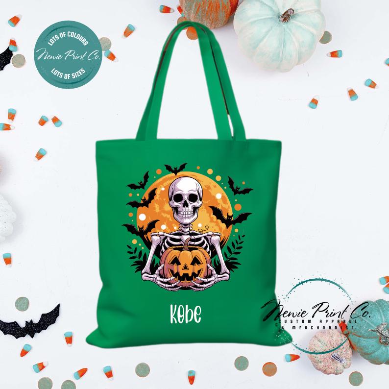 Custom Halloween tote bag with a skeleton holding a pumpkin and a big orange moon and bats behind him, optional personalised name printed on the front, perfect for trick-or-treating or spooky season gifts printed in Australia.