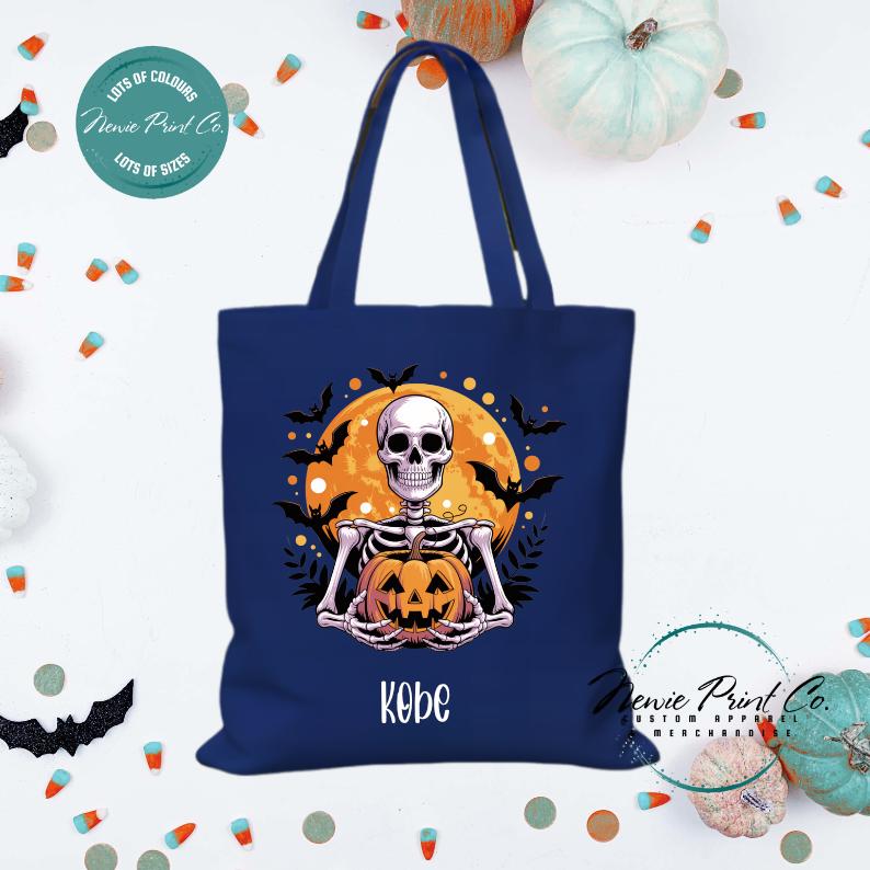Custom Halloween tote bag with a skeleton holding a pumpkin and a big orange moon and bats behind him, optional personalised name printed on the front, perfect for trick-or-treating or spooky season gifts printed in Australia.