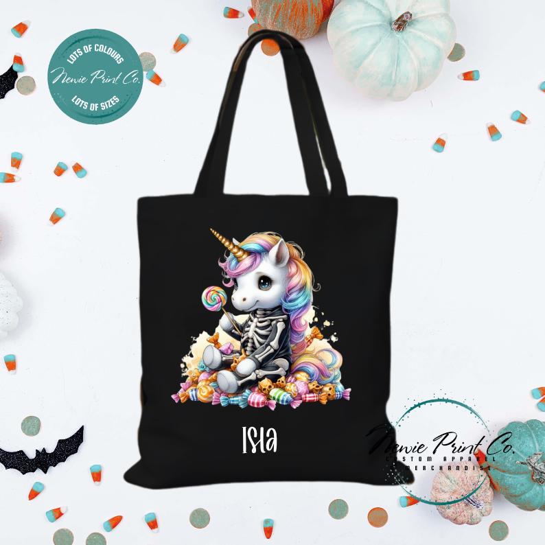 Custom Halloween tote bag with unicorn dressed as a skeleton surrounded by lollies and candy, optional personalised name printed on the front, perfect for trick-or-treating or spooky season gifts