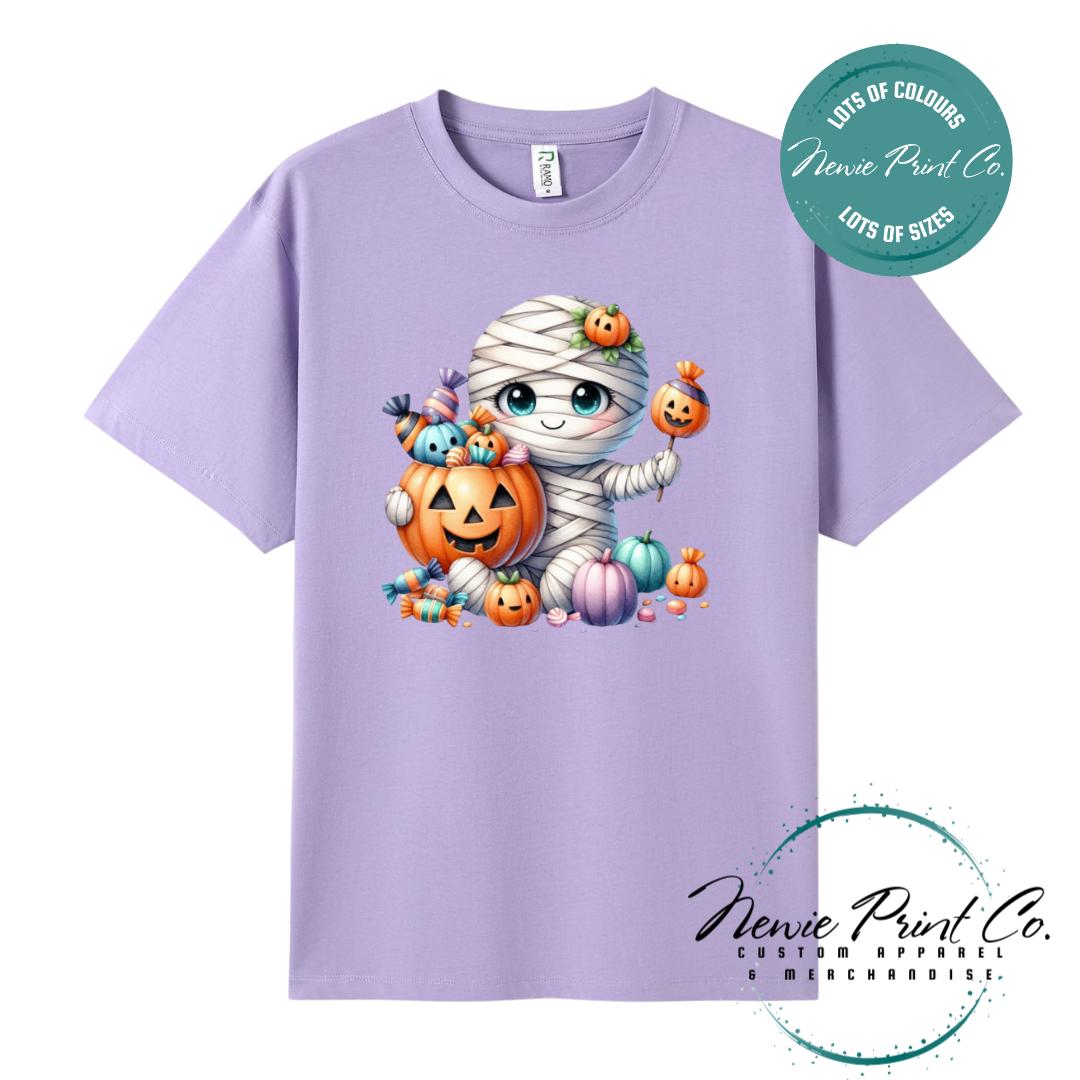 Custom Halloween t-shirts printed in Australia, featuring a cute and spooky mummy holding a pumpkin full of bright coloured candy and optional personalised names — perfect for Halloween parties, school events, or family matching outfits.