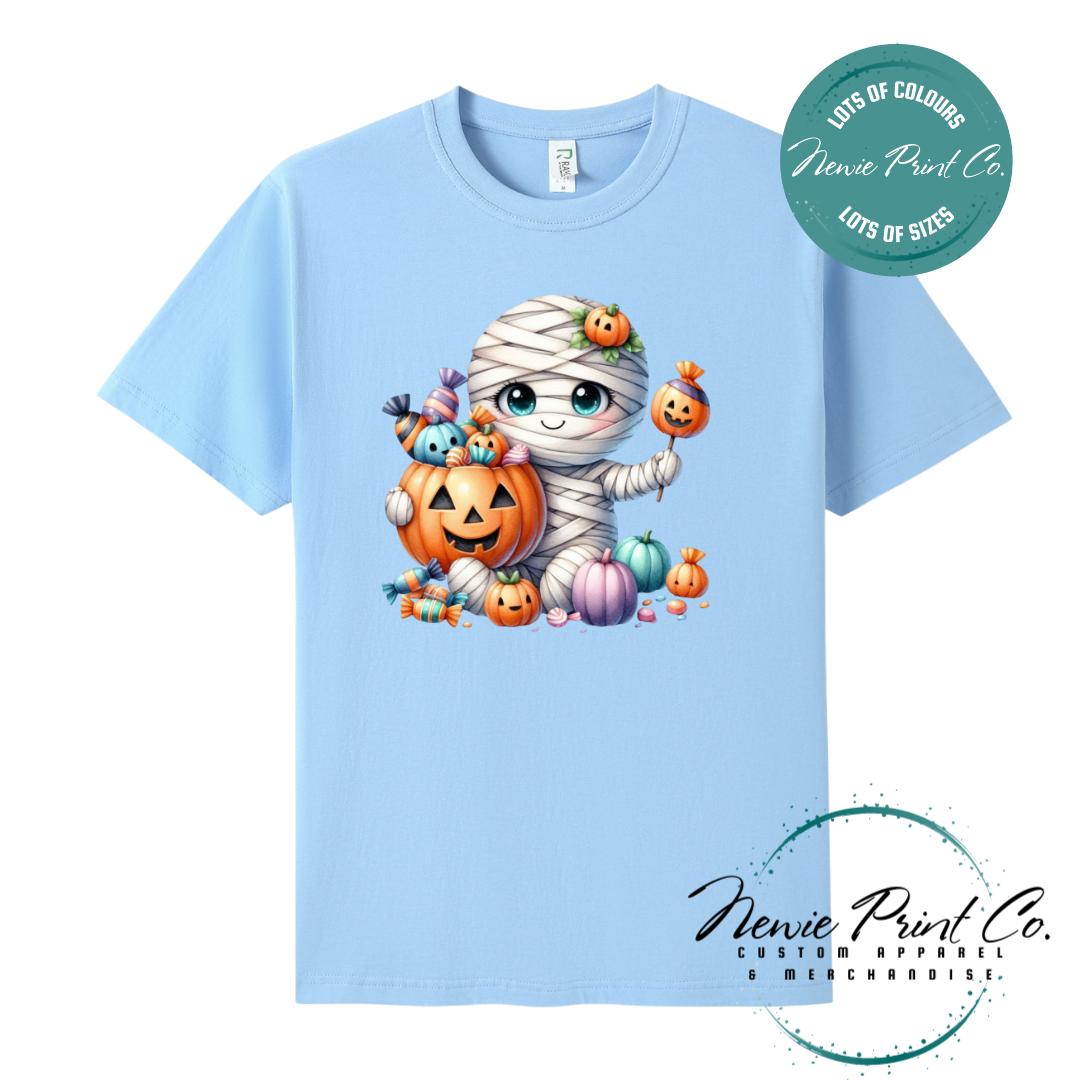 Custom Halloween t-shirts printed in Australia, featuring a cute and spooky mummy holding a pumpkin full of bright coloured candy and optional personalised names — perfect for Halloween parties, school events, or family matching outfits.