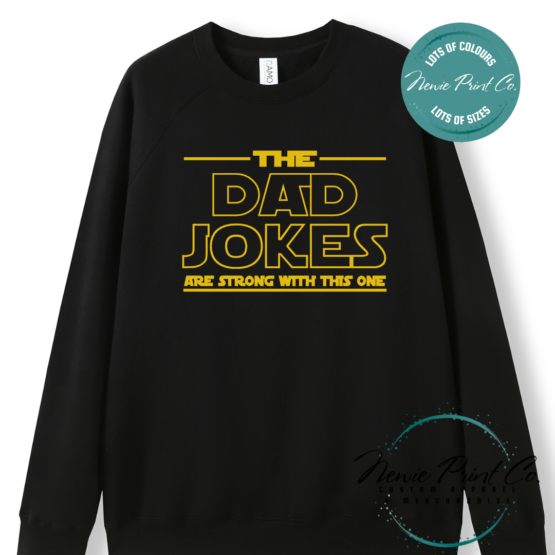 Funny t-shirt and jumper with the text “The Dad Jokes Are Strong With This One”. Humorous Star Wars-inspired quote printed on 100% cotton apparel using high-quality DTF/DTG print. Perfect gift for dads, Father’s Day, or star wars lovers.