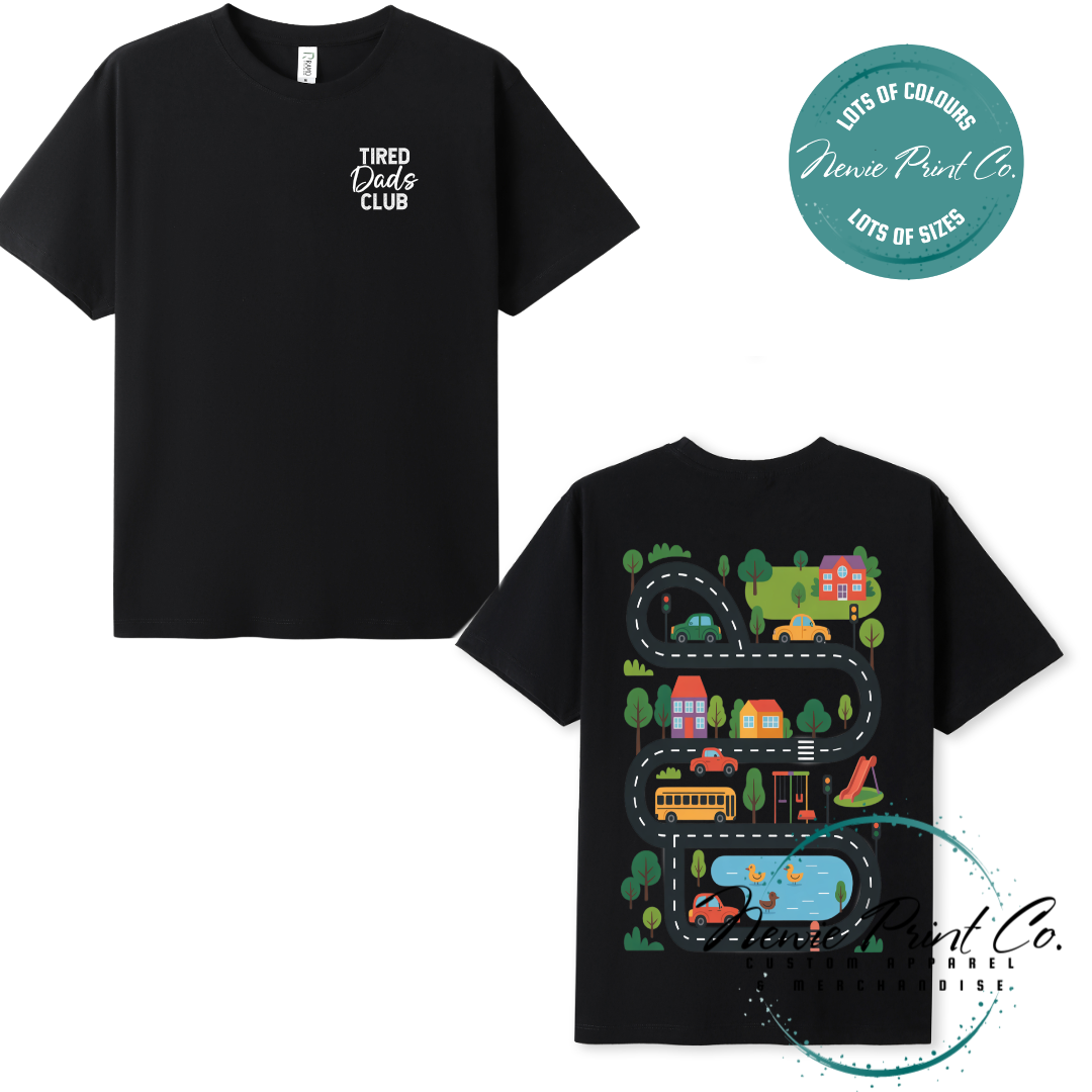Tired Dads Club black t-shirt featuring front text and a vibrant town-themed illustration on the back with houses, vehicles, and winding roads. Available in multiple t-shirt colors and various jumper options. Designed and printed by Newie Print Co.