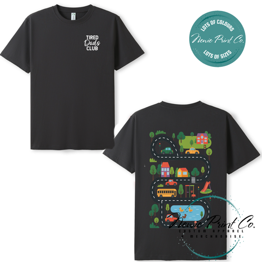 Tired Dads Club black t-shirt featuring front text and a vibrant town-themed illustration on the back with houses, vehicles, and winding roads. Available in multiple t-shirt colors and various jumper options. Designed and printed by Newie Print Co.