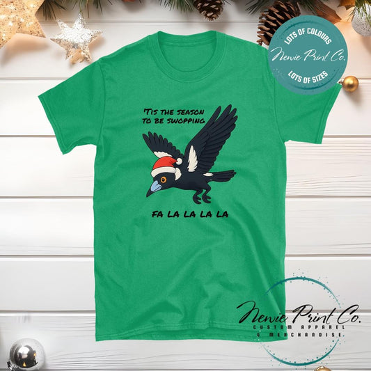 Christmas t-shirt featuring a cartoon magpie wearing a Santa hat with the text ‘’Tis the season to be swooping, fa la la la la.’ Available in multiple colours and sizes from Newie Print Co.