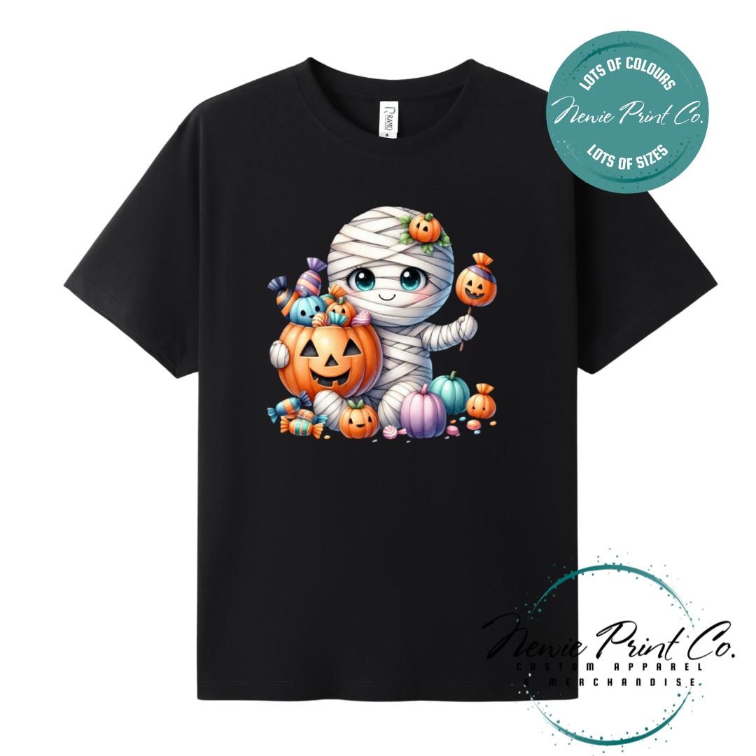 Custom Halloween t-shirts printed in Australia, featuring a cute and spooky mummy holding a pumpkin full of bright coloured candy and optional personalised names — perfect for Halloween parties, school events, or family matching outfits.