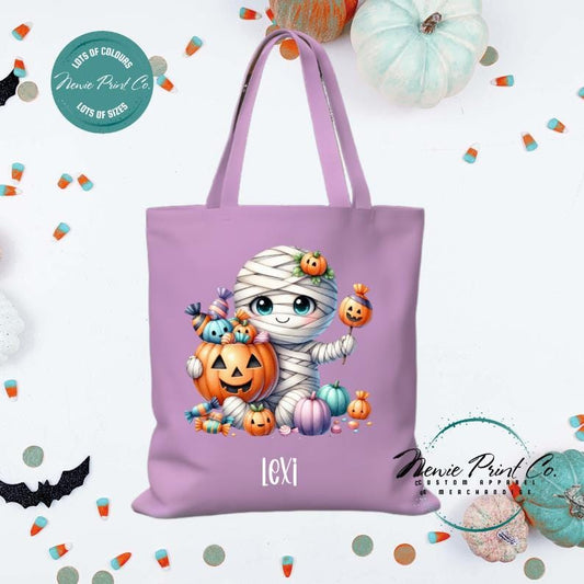 Custom Halloween tote bag with a cute mummy with candy and pumpkins, optional personalised name printed on the front, perfect for trick-or-treating or spooky season gifts printed in Australia by Newie Print Co.
