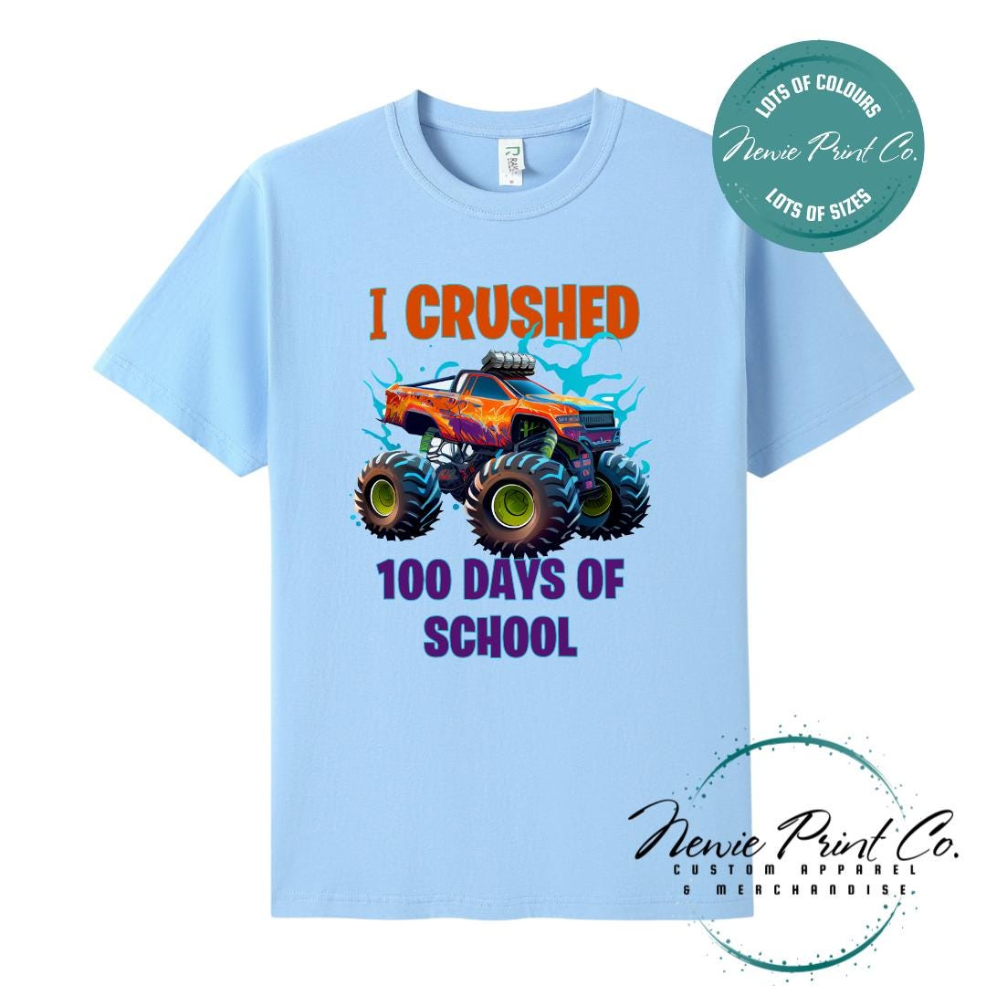 Sky Blue 100 Days of School t-shirt featuring a bold monster truck graphic with the text “I Crushed 100 Days of School,” designed for students or teachers to celebrate the 100th day of school milestone in a fun, playful way. Available in both adult and kids sizes.