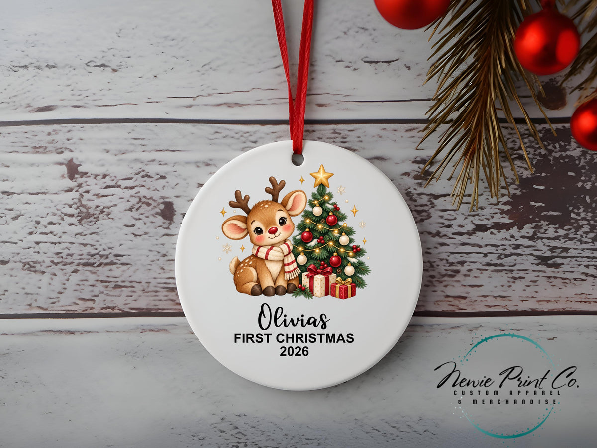 Personalised My First Christmas ornament featuring a cute illustrated reindeer wearing a striped scarf beside a decorated Christmas tree and wrapped presents.