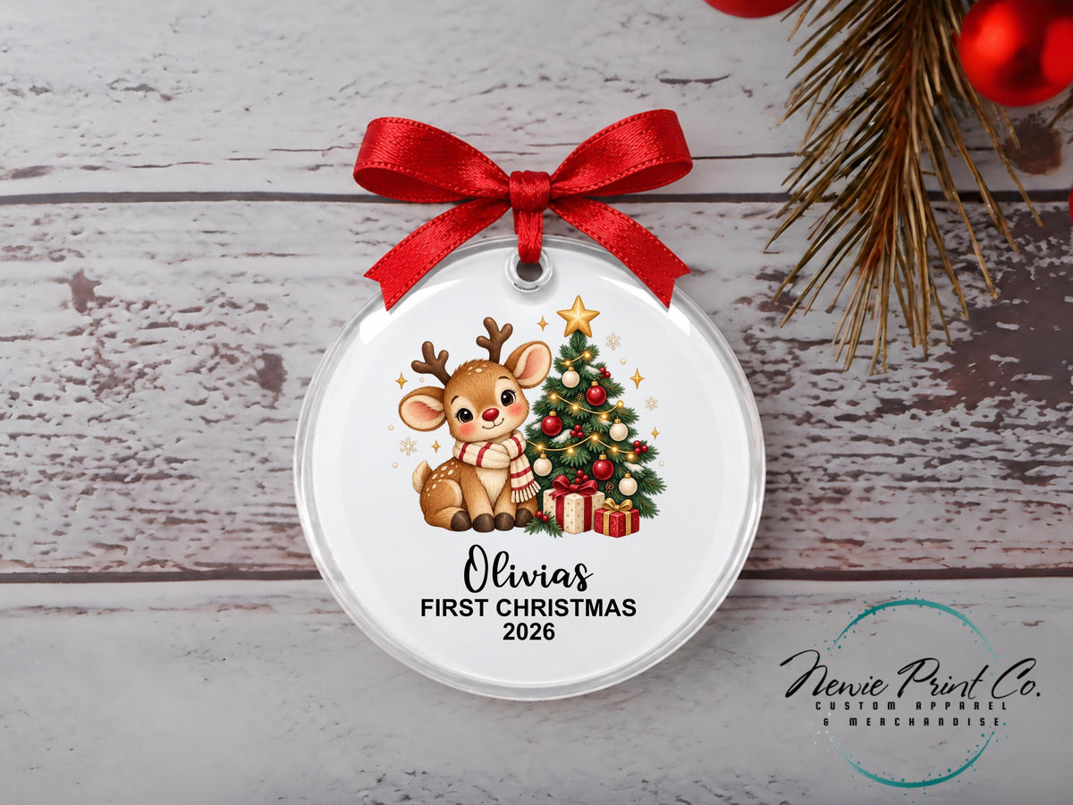 Personalised My First Christmas ornament featuring a cute illustrated reindeer wearing a striped scarf beside a decorated Christmas tree and wrapped presents.