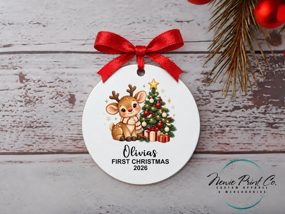 Personalised My First Christmas ornament featuring a cute illustrated reindeer wearing a striped scarf beside a decorated Christmas tree and wrapped presents.